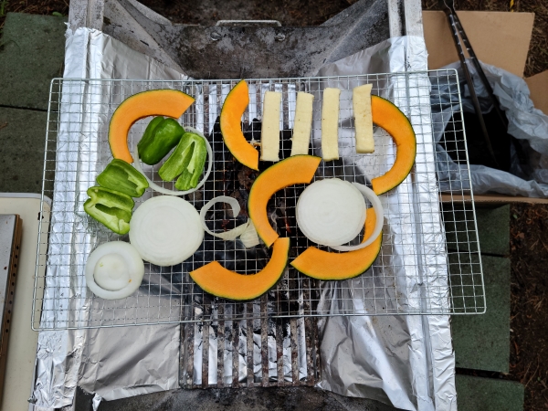 Sliced pumpkin, onions, green peppers, and feta cheese on a barbecue grill.