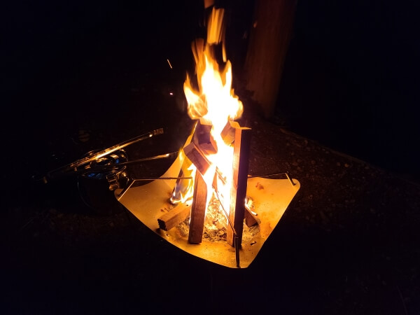 A bright wooden campfire in the center of a dark picture.