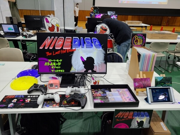 Nice Gear Games booth with Nice Disc and monitor on the left and Indie Tsushin and print copies on the right.