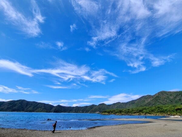 A huge blue sky scattered with thin clouds. Underneath is an equally blue lake edged with green mountains.