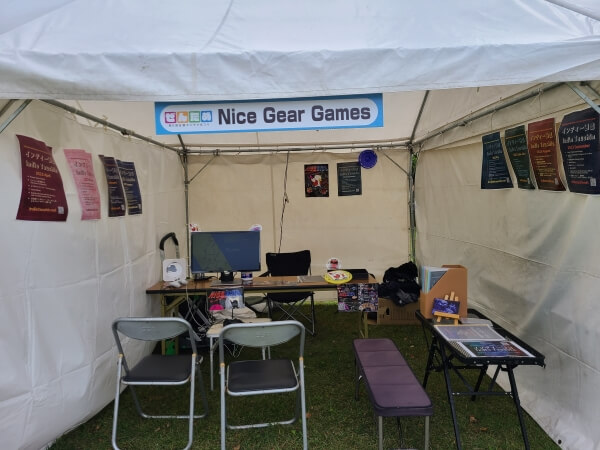 Nice Gear Games tent at Zentame with Nice Disc set up on one side and a readng area for Indie Tsushin on another. Colorful posters of the Indie Tsushin zine covers hang on the walls.